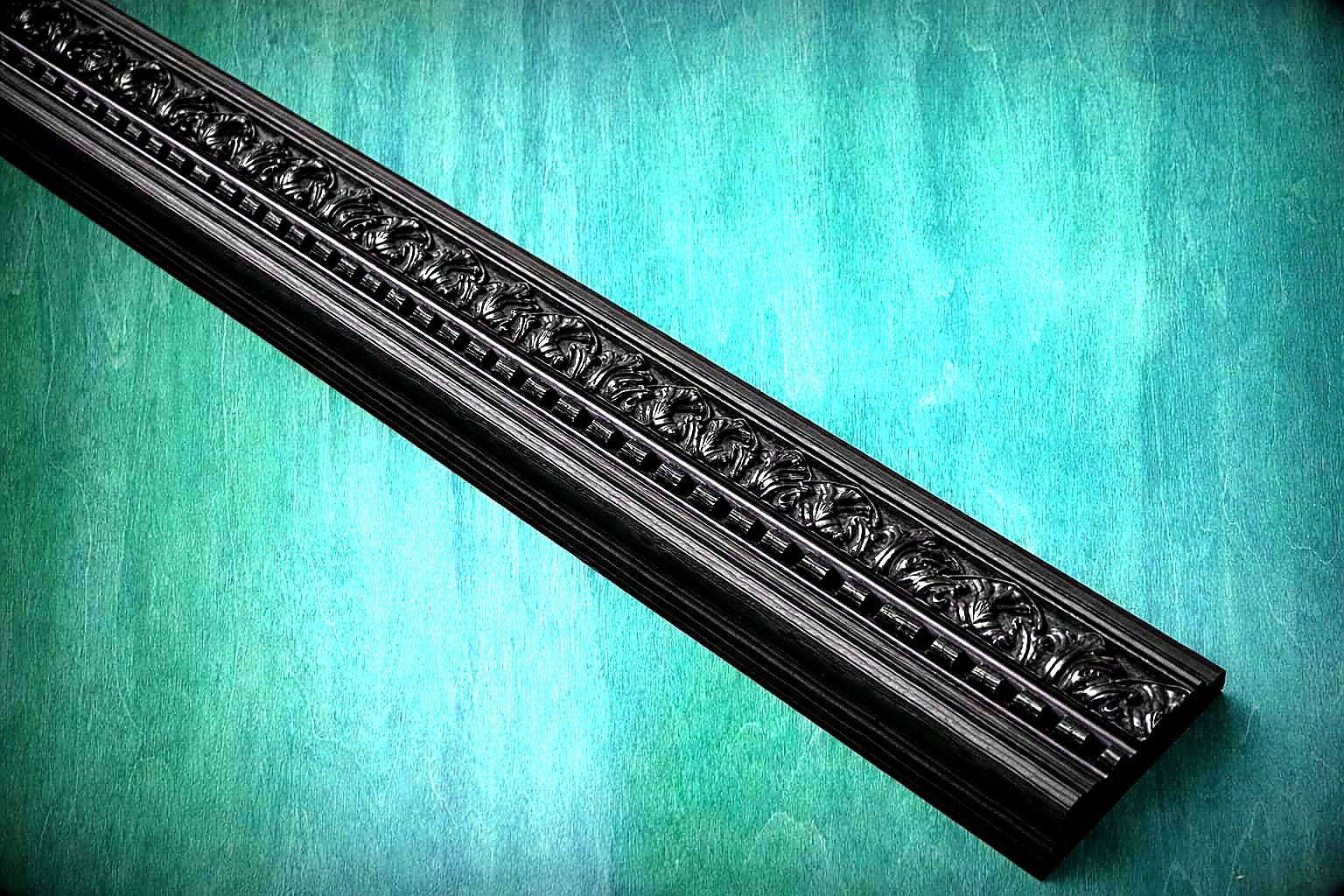 Workshop detail — the ornate dentil cornice with carved acanthus leaf moulding before fitting, photographed against teal backdrop